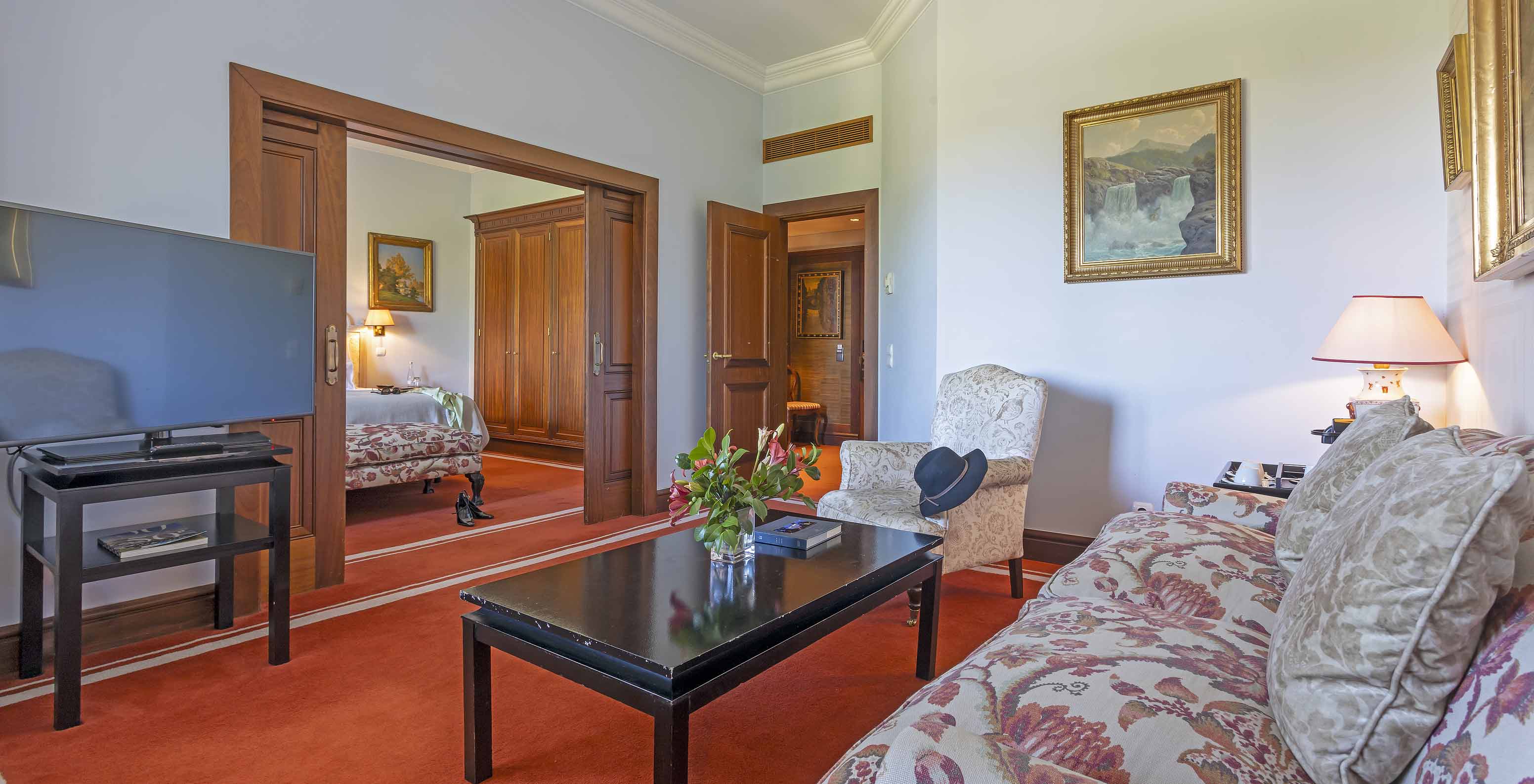 The Suite at Pestana Palace Lisboa has a living room with a sofa and an armchair, a coffee table, and a television