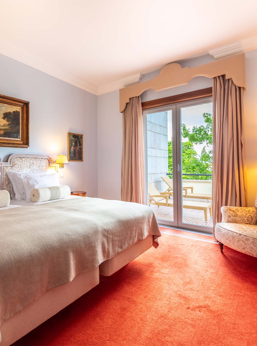 The Suite Collection at Pestana Palace Lisbon has a double bed, an armchair, a desk, and a window with access to the garden