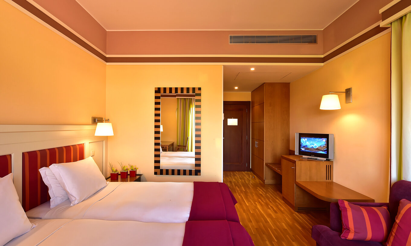 The Classic Double of Pestana Sintra Golf has two beds, a mirror on the wall, and a unit with a small television