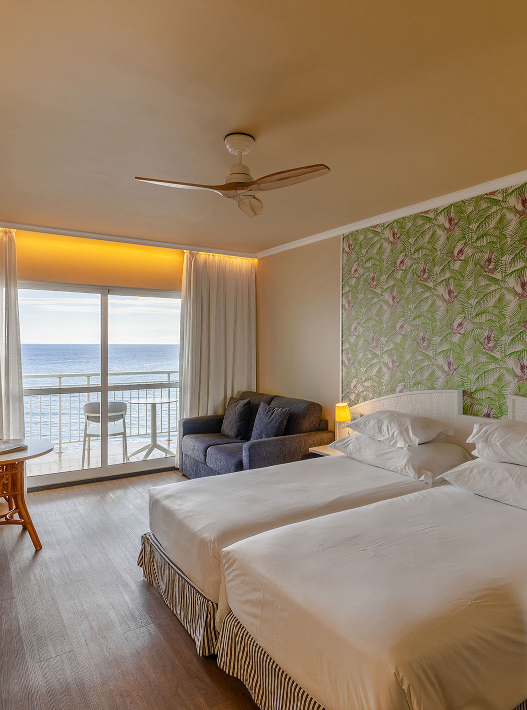 The Pestana Ocean Bay All Inclusive Premium Sea View has a double bed, palm tree wallpaper, a sofa, and a balcony