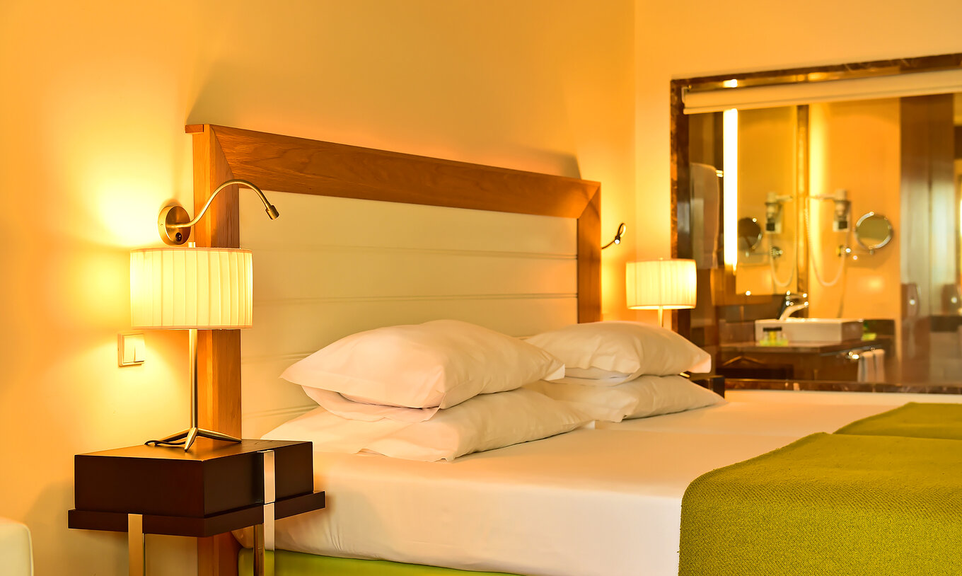 The Classic of Pestana Promenade has a bed with a green bedspread, lamps on the nightstand, and a bathroom at the back
