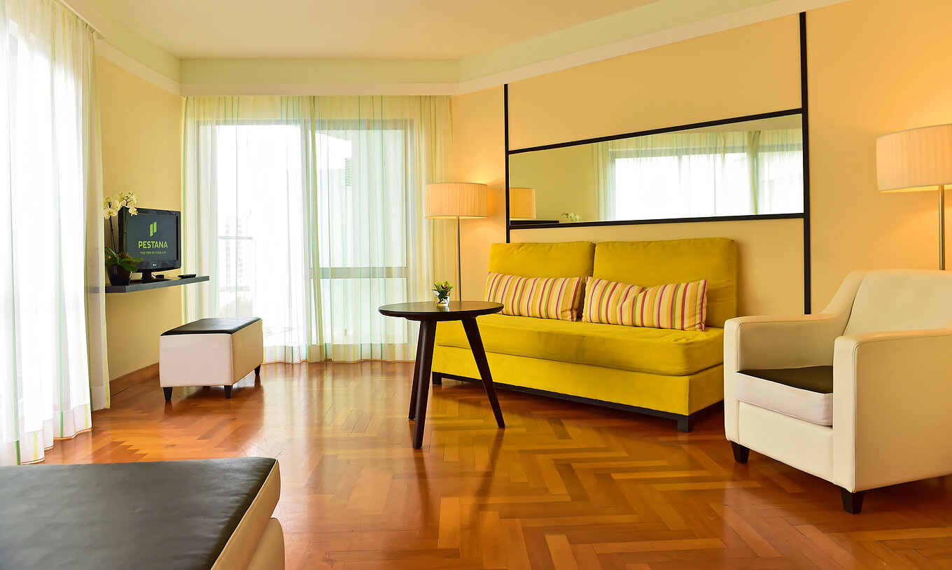 The Classic of Pestana Promenade has a living room with a green sofa, an armchair, and a television on a shelf