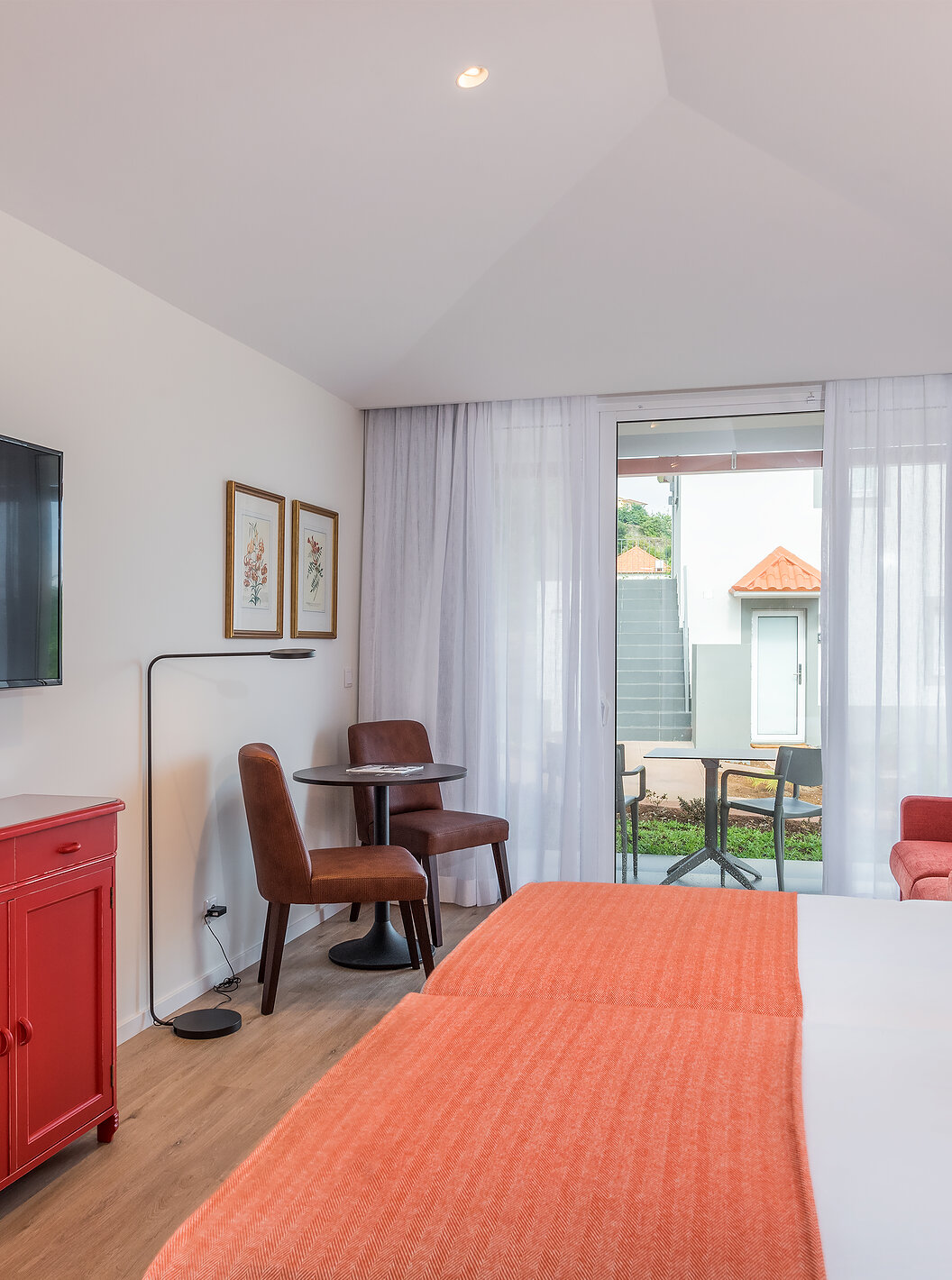 The Sea View Studio of Pestana Quinta do Arco has two joined beds, television, red sofa, and balcony with table and chairs