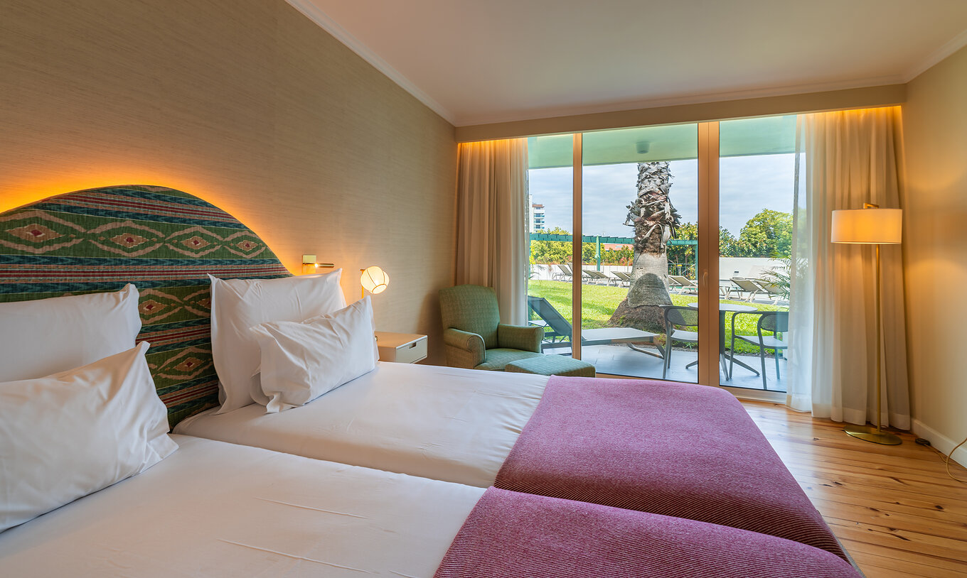 The Pool View Room at Pestana Quinta Perestrello has a double bed with a pink bedspread and a balcony with a view.