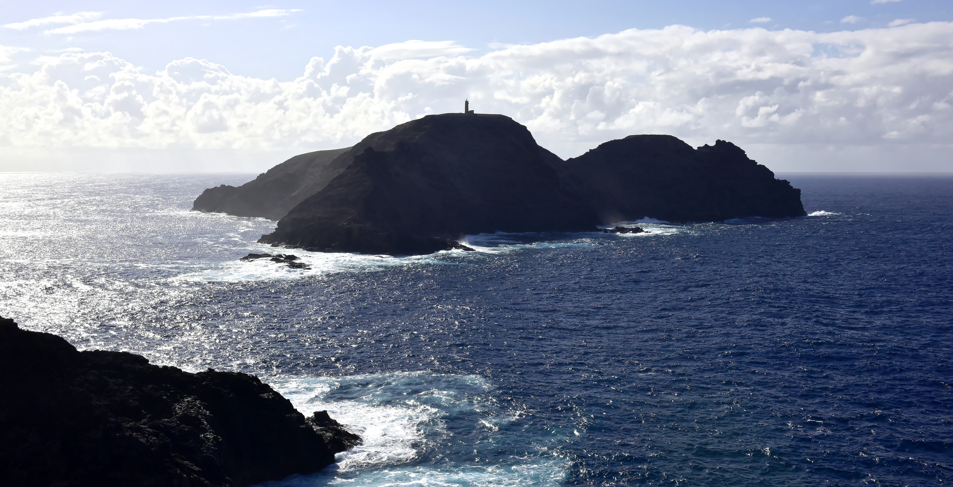 Lighthouse on Ilhéu de Porto Santo, a rocky island surrounded by deep blue sea and a sky with white and gray clouds