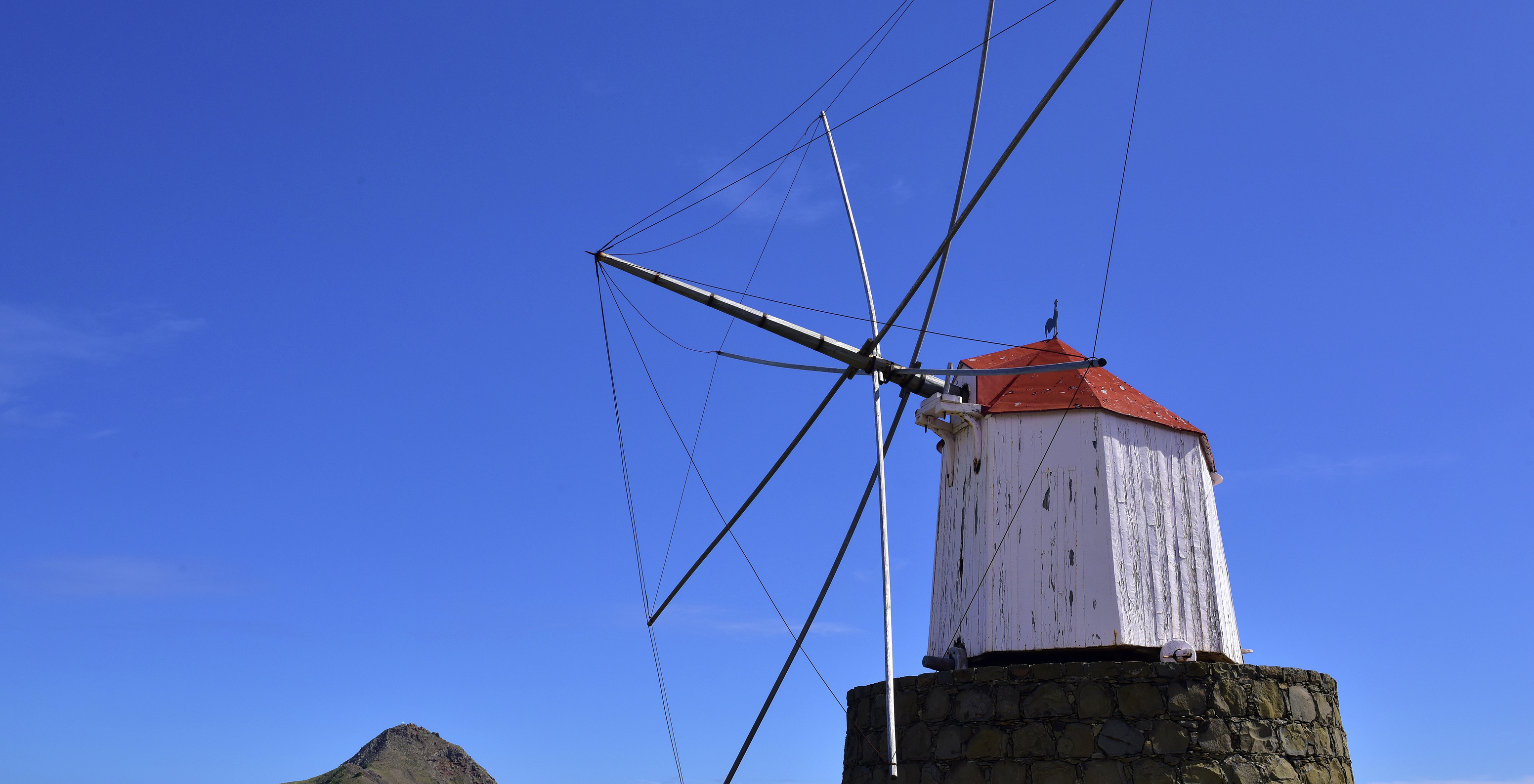 White windmill in Porto Santo, standing against vibrant blue sky and surrounded by a green hill