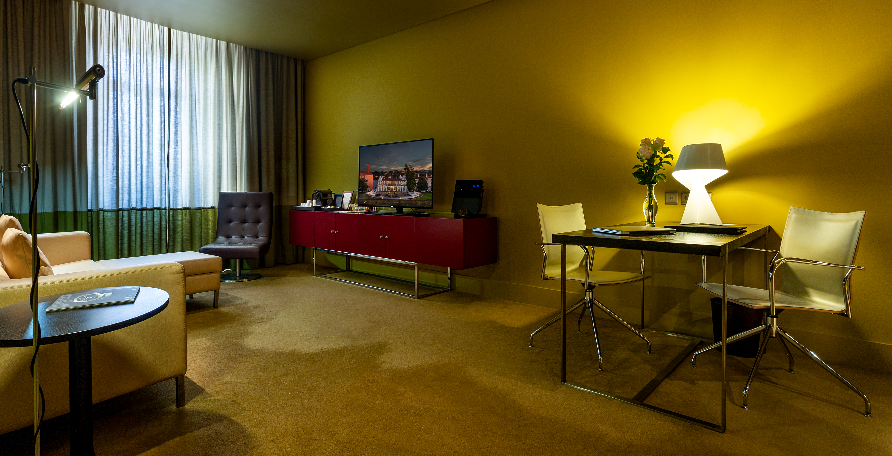 The Junior Suite of Pestana Palácio do Freixo has a table with two chairs, a sofa, TV and a window with curtains