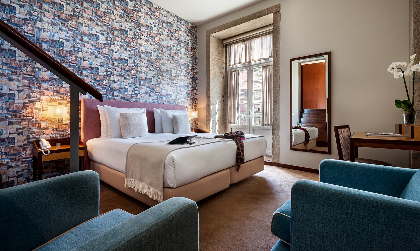 The Plaza room at Pestana Vintage Porto has a double bed, wallpaper with travel photographs, and an armchair
