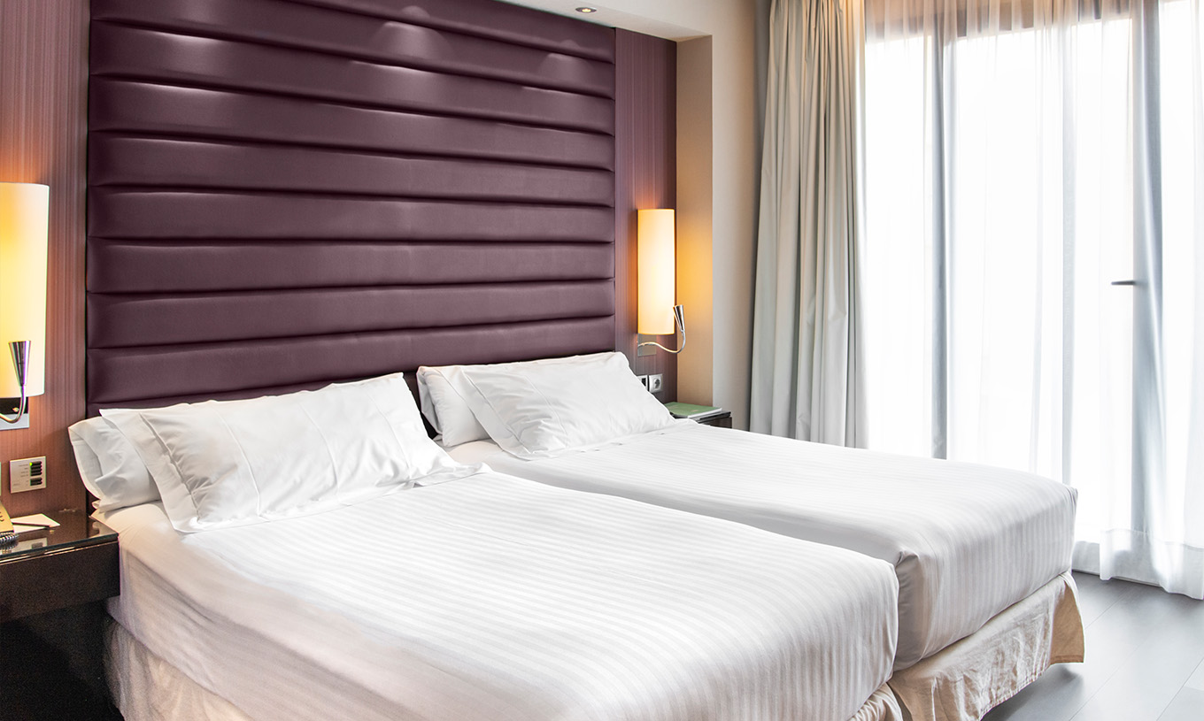 Premium Room at Pestana Arena Barcelona featuring twin beds, tall padded headboard and sheer window curtains