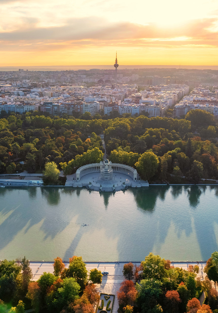 Madrid resort with an aerial view over El Retiro Park lake, tree lined avenues and skyline at sunset