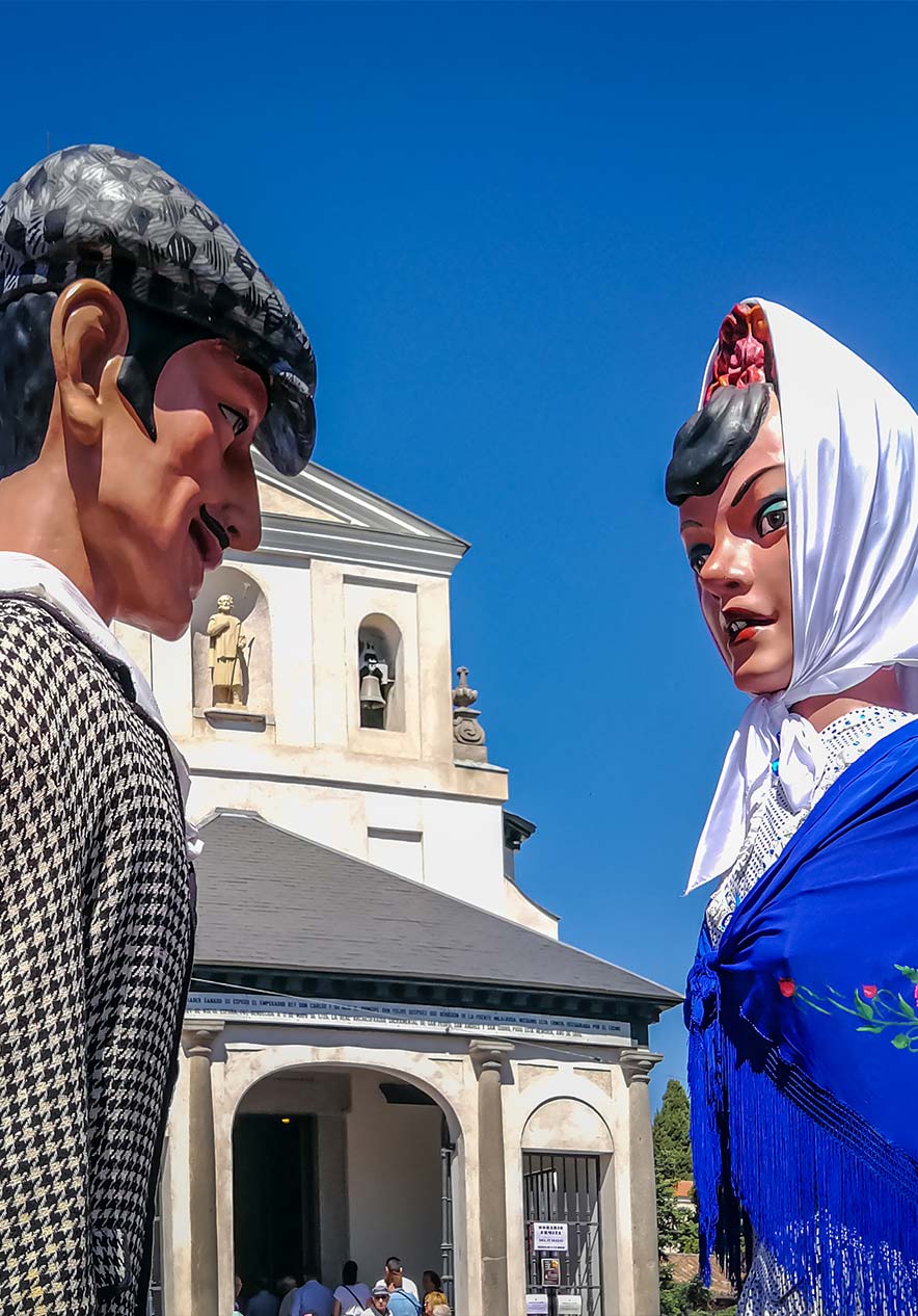 San Isidro festival figures beside a historic church in Madrid beneath a clear blue summer sky during a local celebration