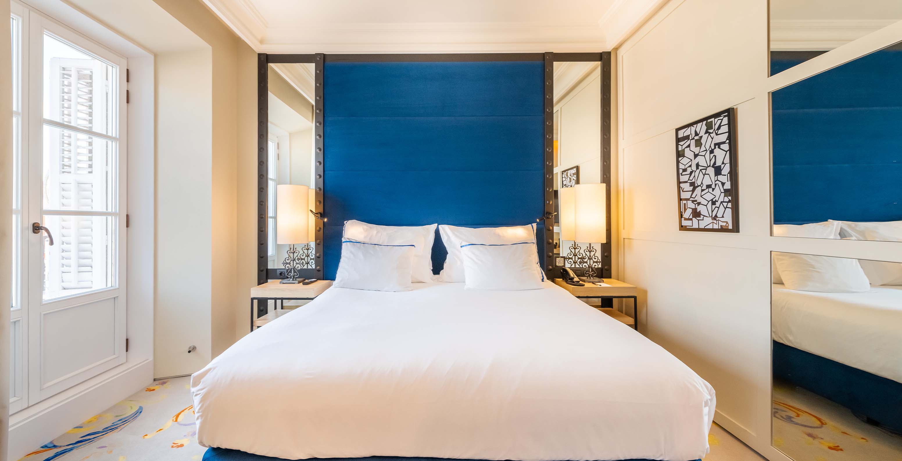 The Superior Plaza Mayor at Pestana Plaza Mayor Madrid has a double bed with blue headboard with mirror and a large window
