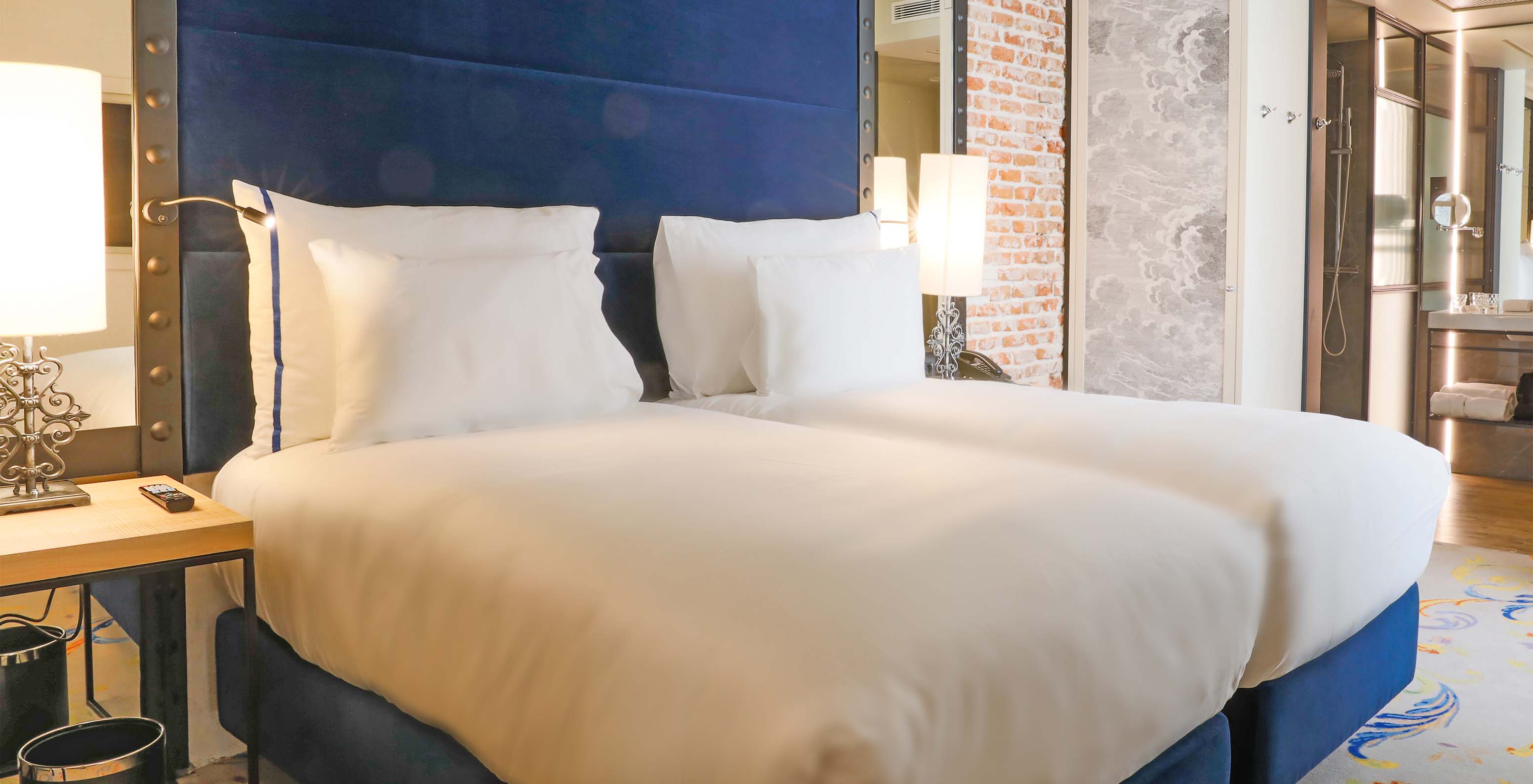 The Superior Room at Pestana Plaza Mayor Madrid has two beds with blue headboard and a wall with bricks