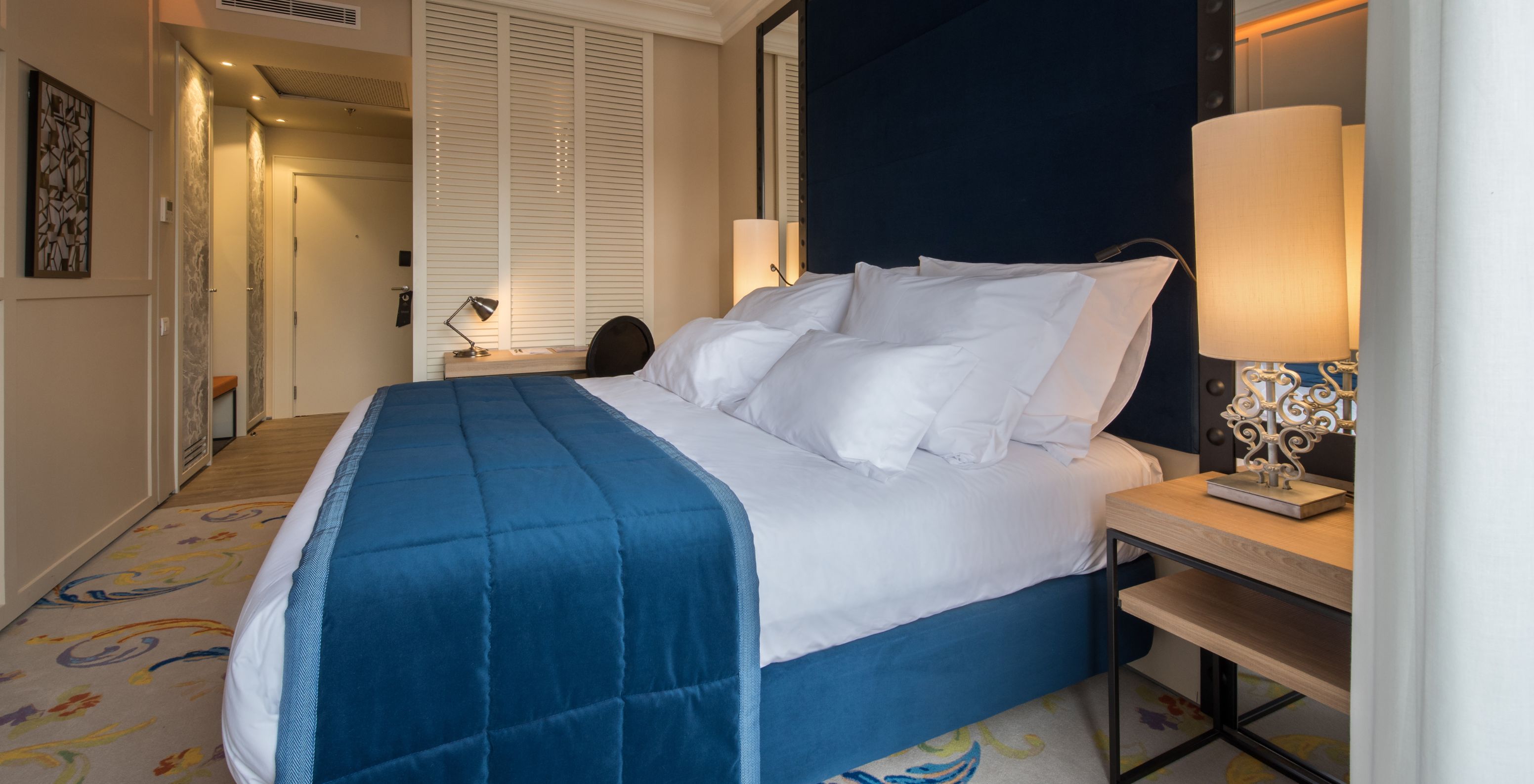 The Superior Plus Room at Pestana Plaza Mayor Madrid has a double bed with a blue bedspread and a rug.
