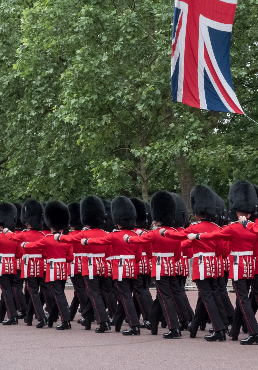 Trooping the Colour guards marching beneath a Union Jack flag during a ceremonial parade in London with bearskin hats