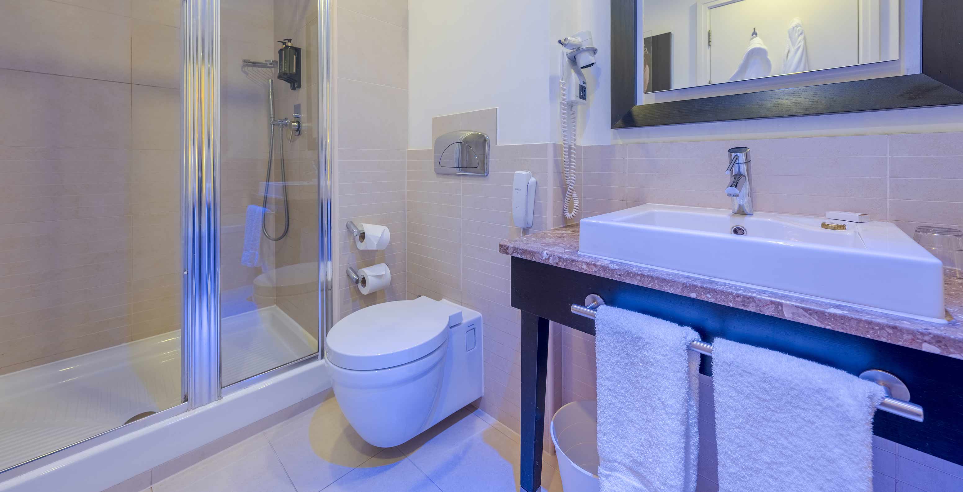 The Superior King at Pestana Chelsea Bridge has a bathroom with glass shower, toilet, sink and mirror