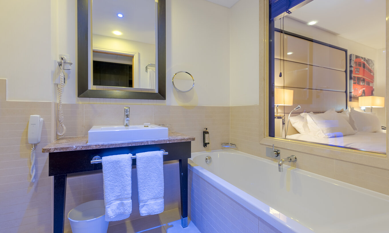 The Deluxe Family at Pestana Chelsea Bridge has a bathroom with bathtub, glass wall, sink, mirrors and hairdryer