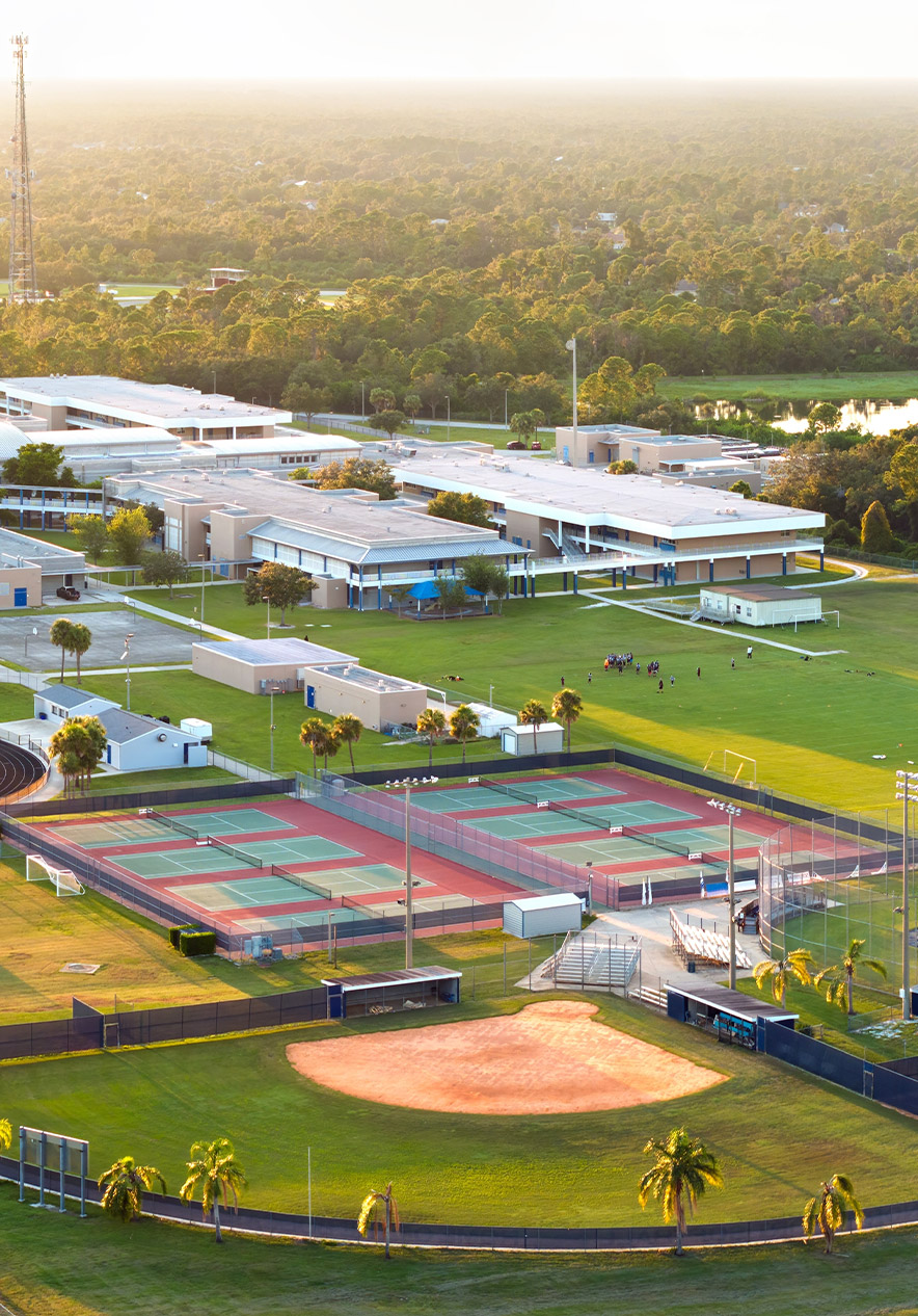 Aerial view of tennis courts, baseball field and school buildings surrounded by trees in warm evening light
