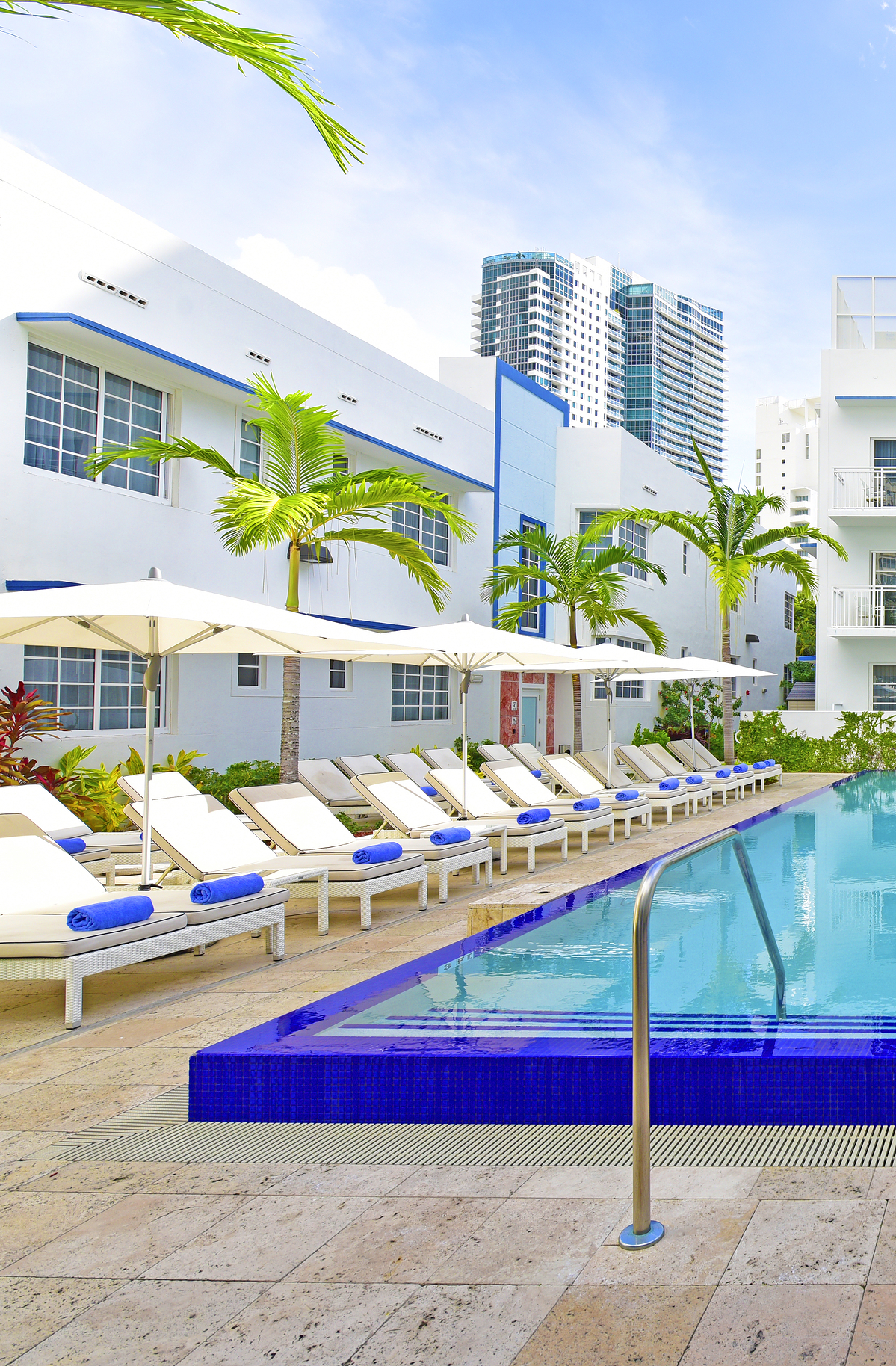 A pool with lounge chairs and umbrellas in front of a white building with blue trim.