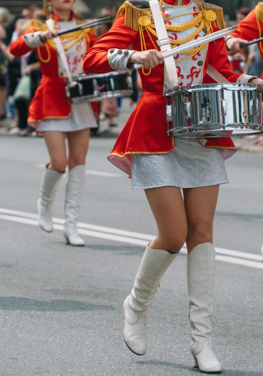 Marching band drummers in red and white parade uniforms performing along a city street during a festive procession