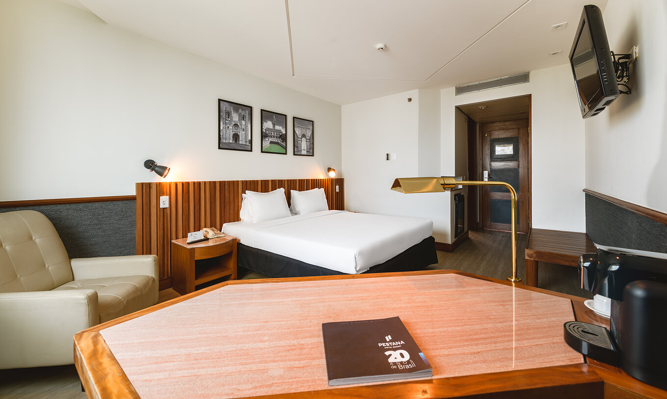 El Deluxe del Pestana São Paulo tiene una cama de matrimonio, televisión, sillón y escritorio con lámpara dorada