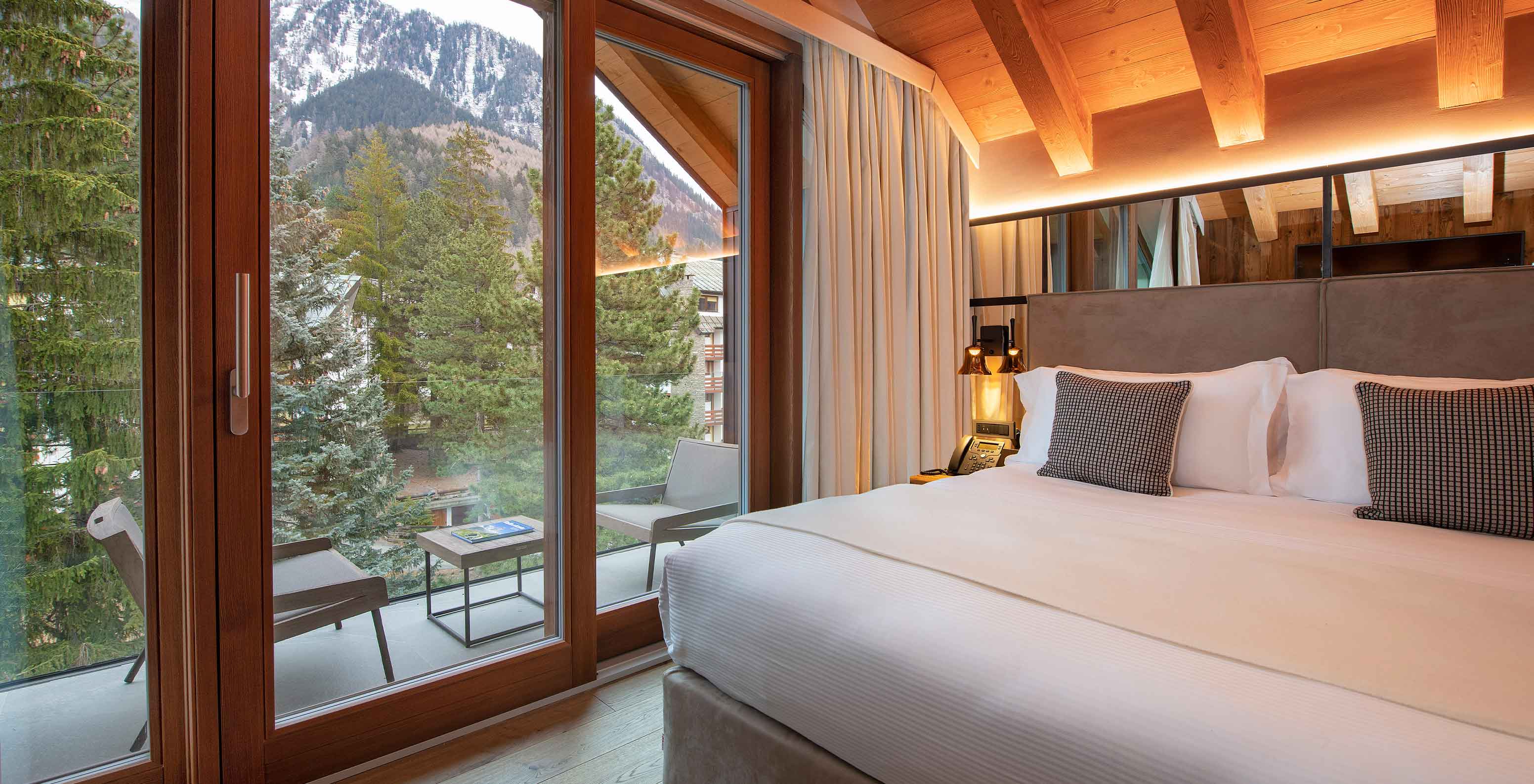 Le Massif Courmayeur, Hotel en los Alpes italianos, con dormitorio de madera y balcón frente a montañas