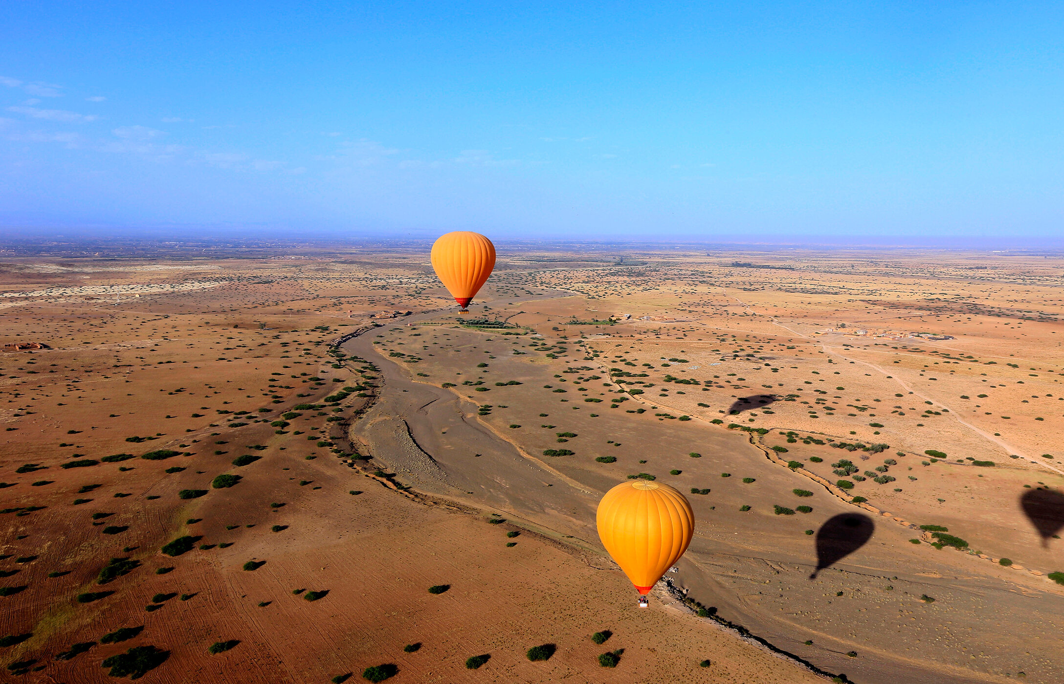 Vista aérea de una llanura cerca de Marrakech, con dos globos aerostáticos naranjas sobrevolando la llanura