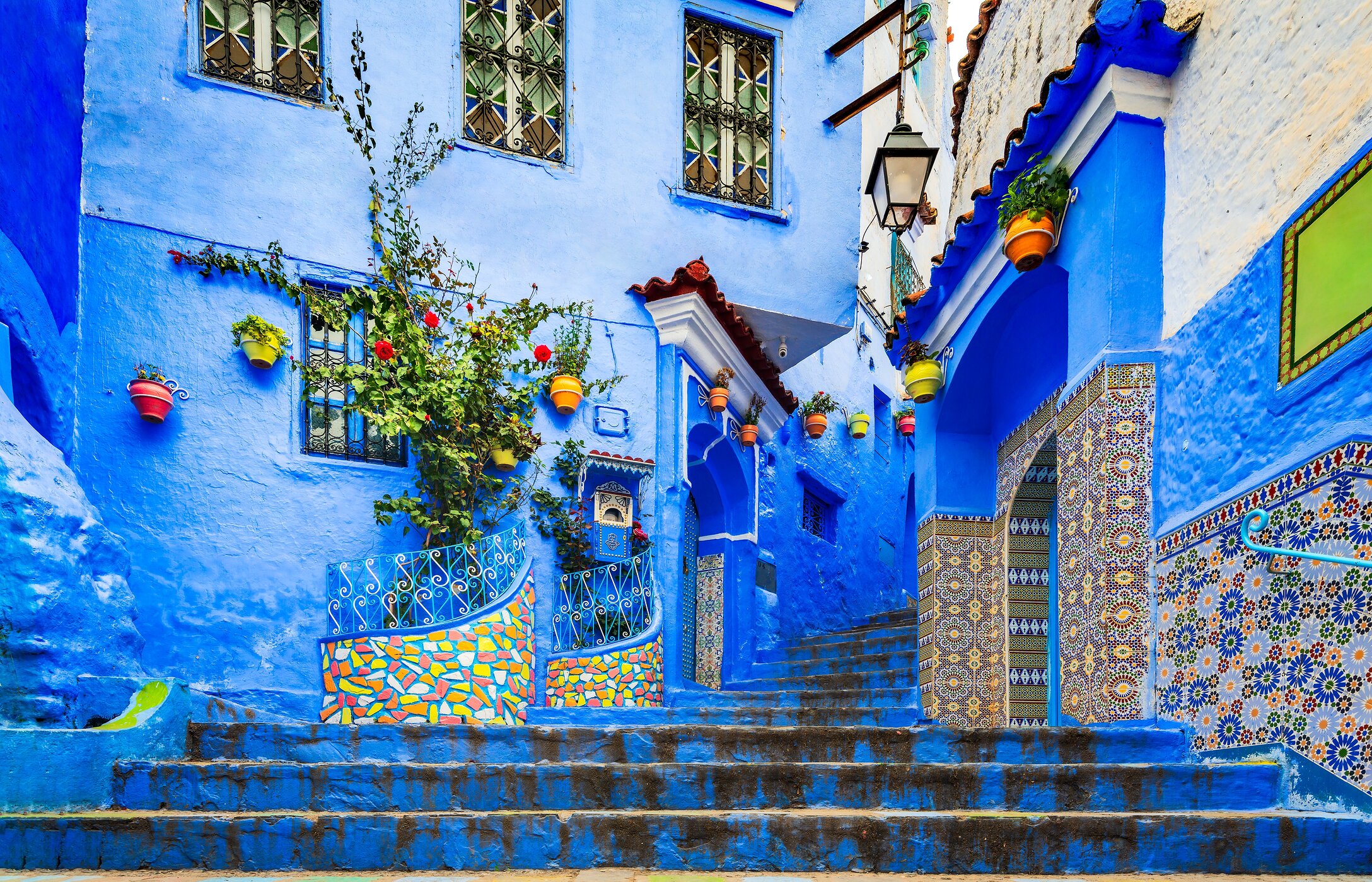 Escalera en Chefchaouen, con edificios azules, azulejos con patrones y macetas colgadas.