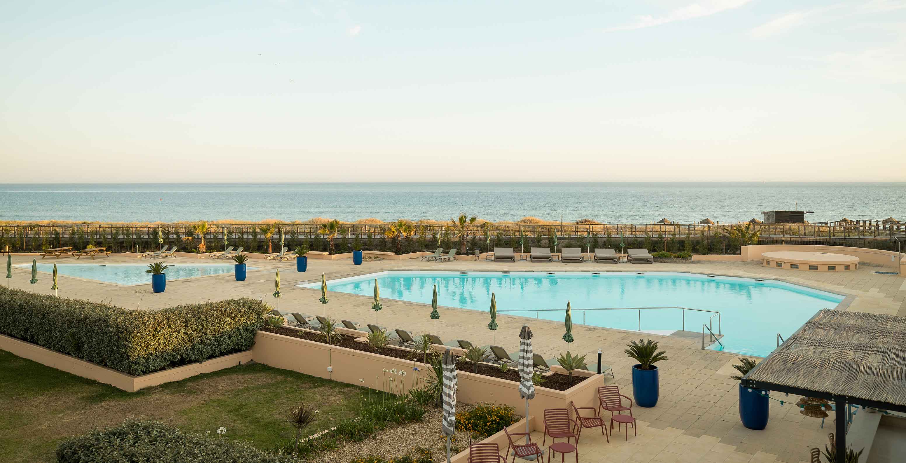 Hotel cerca de la playa con piscina exterior, muchas tumbonas, jardines, vegetación y el mar azul de fondo