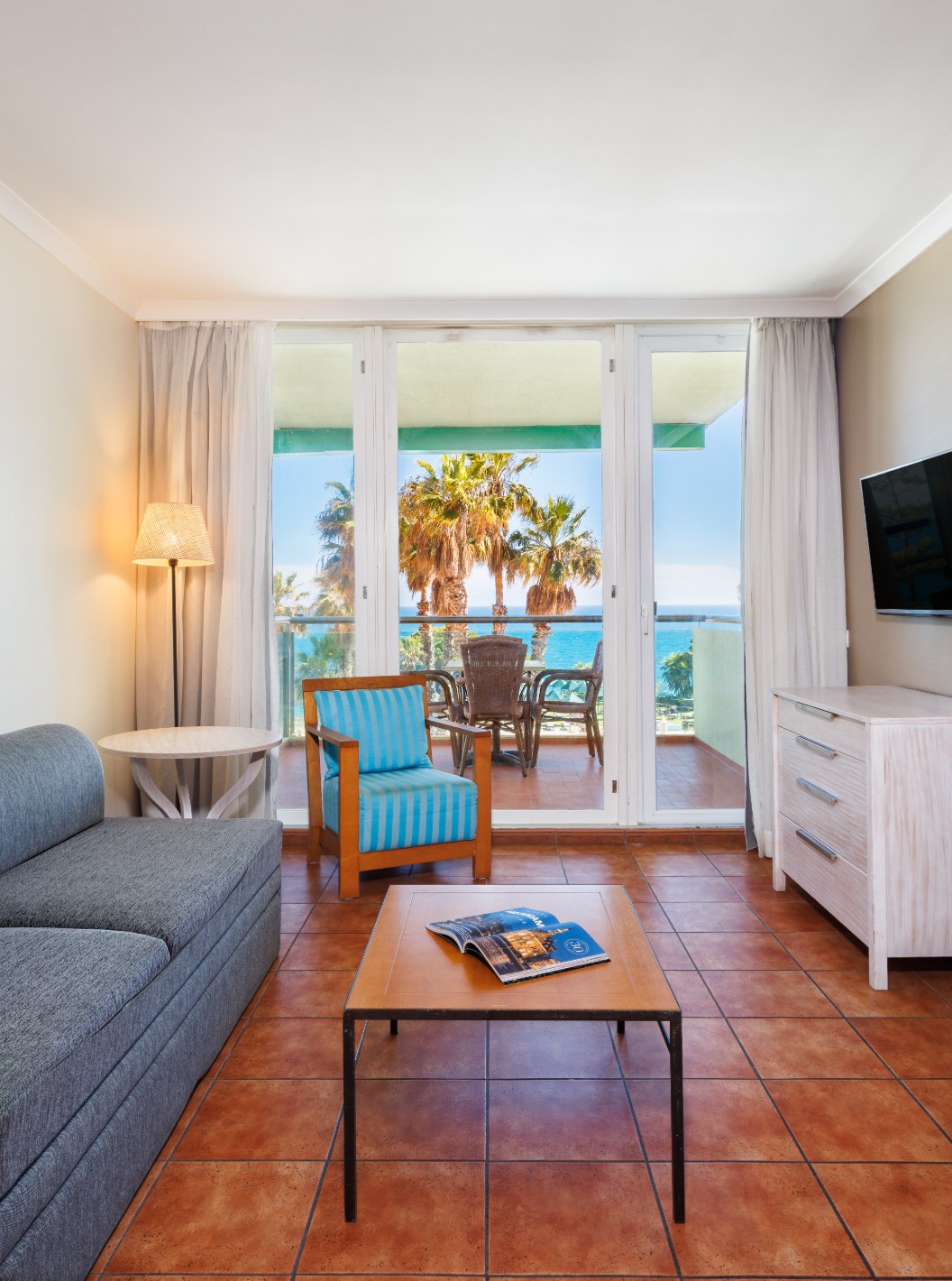 Suite con Vista al Mar en Pestana Viking con sala luminosa, sofá gris y balcón frente al océano con vista de palmeras