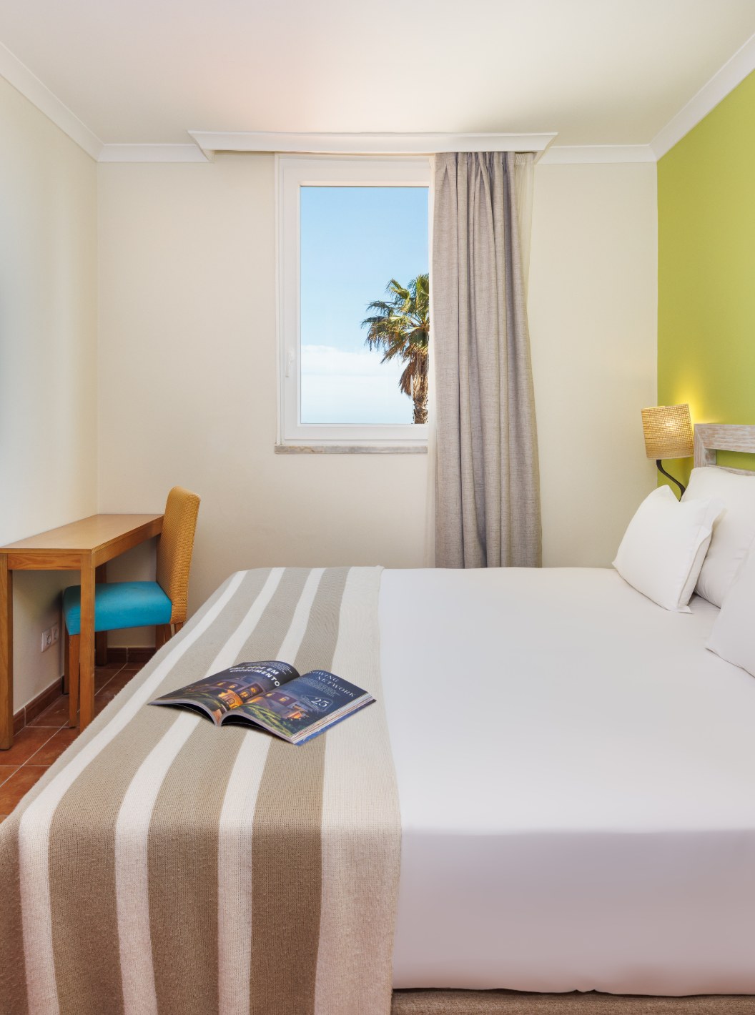Suite T2 con Vista al Mar en Pestana Viking, dormitorio con cama doble, escritorio y ventana con palmera
