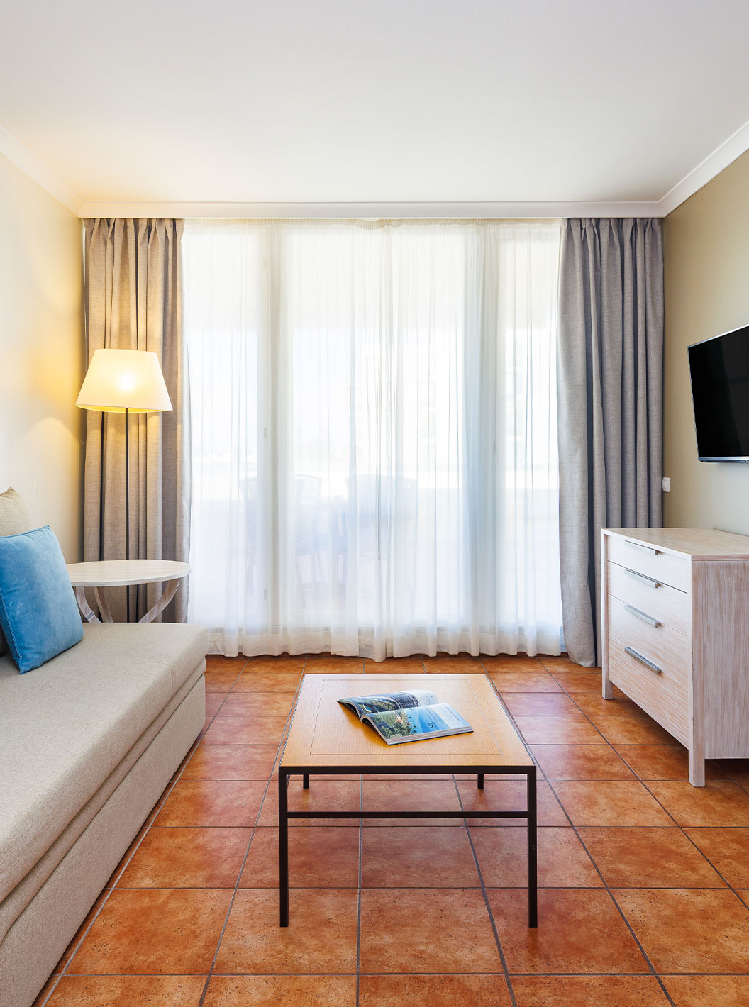 Suite en Pestana Viking con sofá beige, mesa baja, televisor y cortinas junto a un balcón luminoso