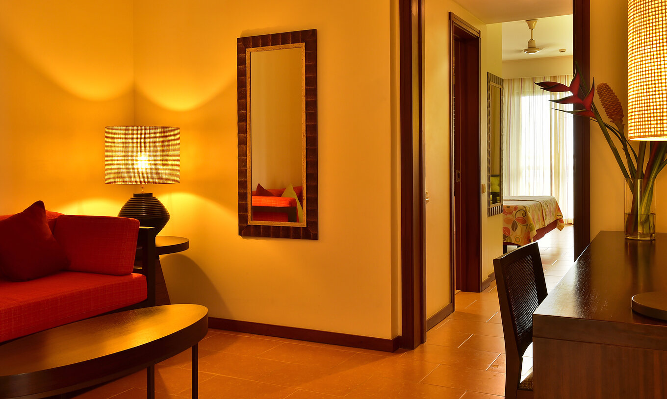 La Junior Suite del Pestana São Tomé tiene una sala con sofá rojo y mesa de centro, y un escritorio con flores decorativas