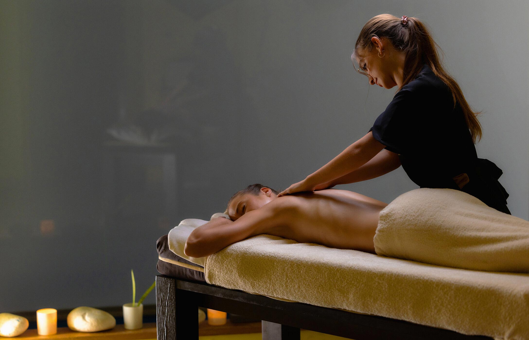 Terapeuta realizando un masaje relajante sobre una camilla en una sala de spa con luz tenue y velas encendidas