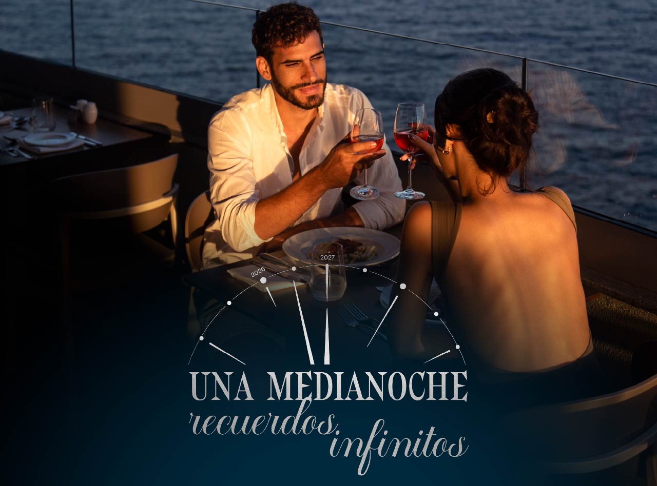 Pareja brinda con copas de vino durante una cena al atardecer frente al mar en una terraza iluminada