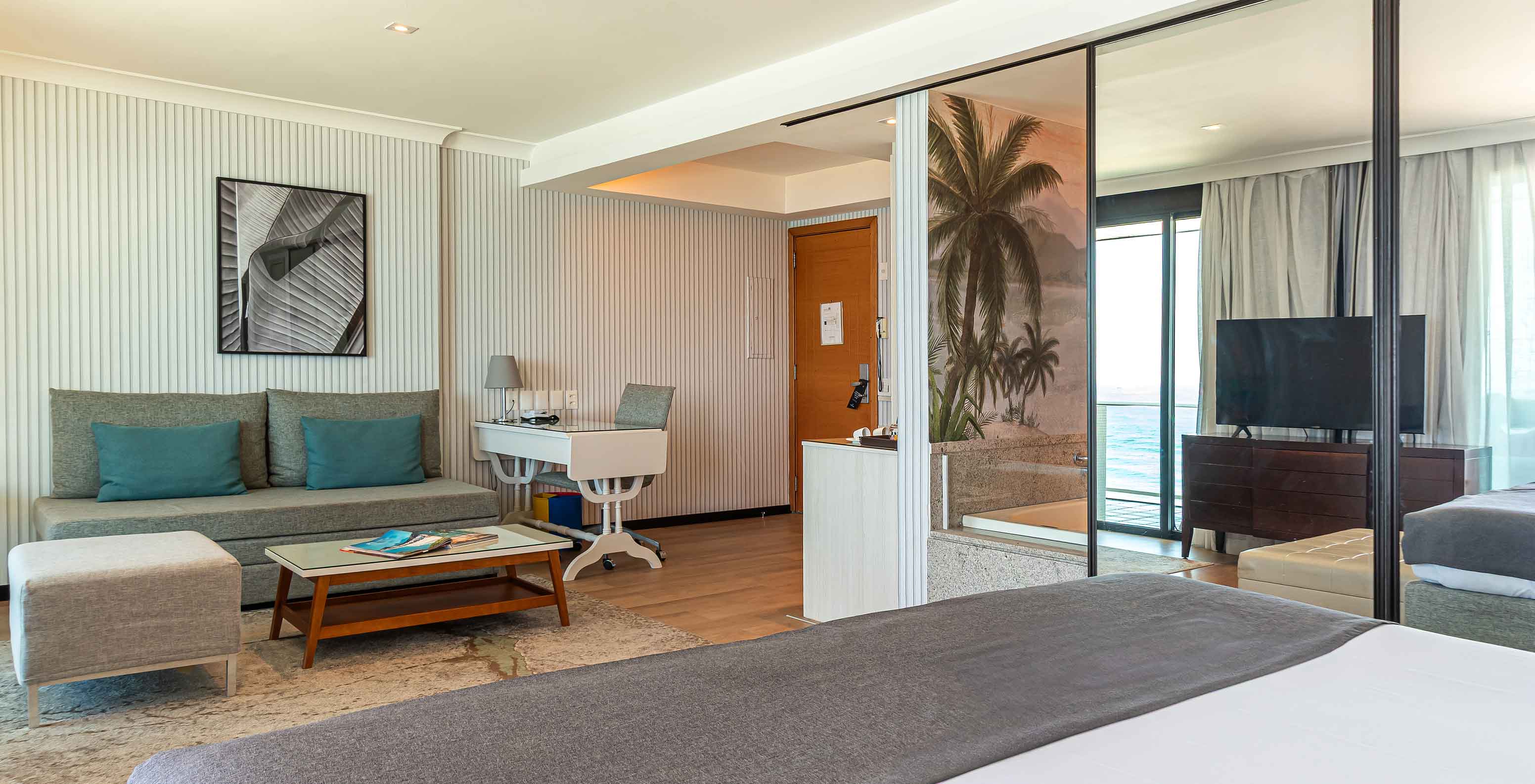 La Suite Oceánica del Pestana Rio Atlântica tiene cuarto moderno con cama, sofá, mesa y TV.