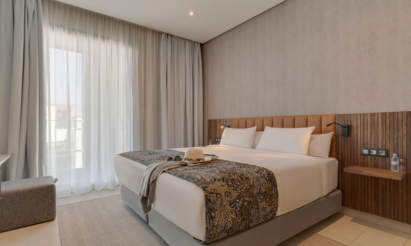 Suite Premium Frente a la Playa en Pestana Casablanca con cama doble, cortinas amplias y pared de madera