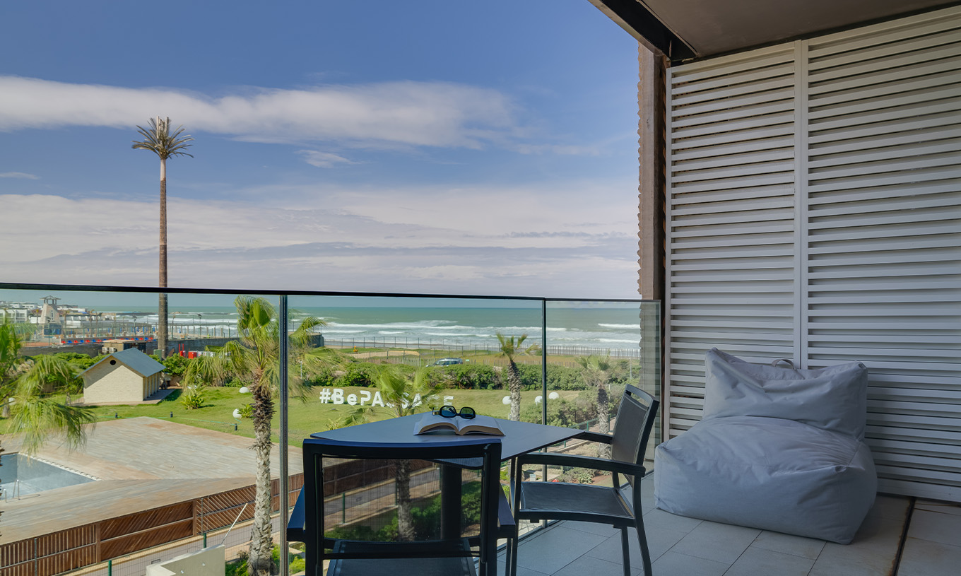 Suite Premium con Vistas Laterales al Océano en Pestana Casablanca, balcón con mesa frente al mar y palmeras