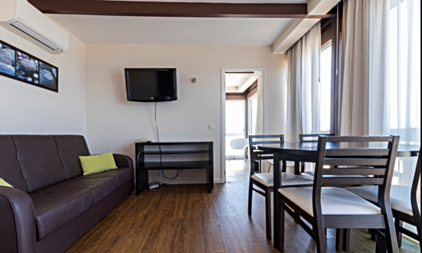 El Estudio Superior Vista Mar del Pestana Alvor Atlântico cuenta con una sala luminosa con sofá, mesa de comedor y televisión, ofreciendo un ambiente acogedor con grandes ventanales que dejan entrar abundante luz natural.