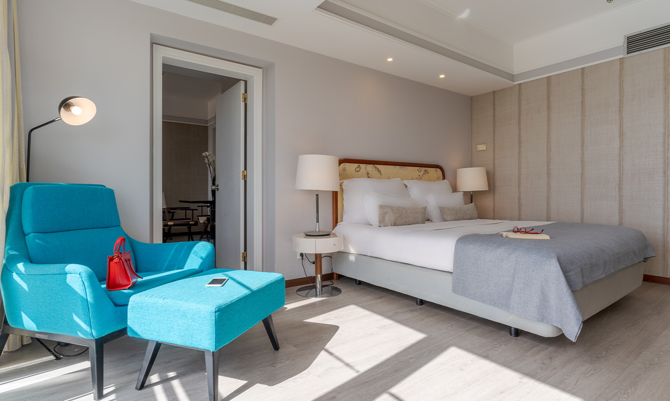 La Suite Vista Mar del Pestana Alvor Praia tiene cama matrimonial con sillón y reposapiés azules, lámparas y suelo de madera