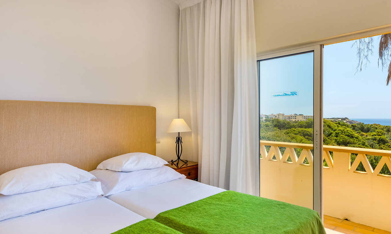El Apartamento T2 Superior del Pestana Palm Gardens tiene dos camas juntas con colcha verde, una terraza con vista al mar