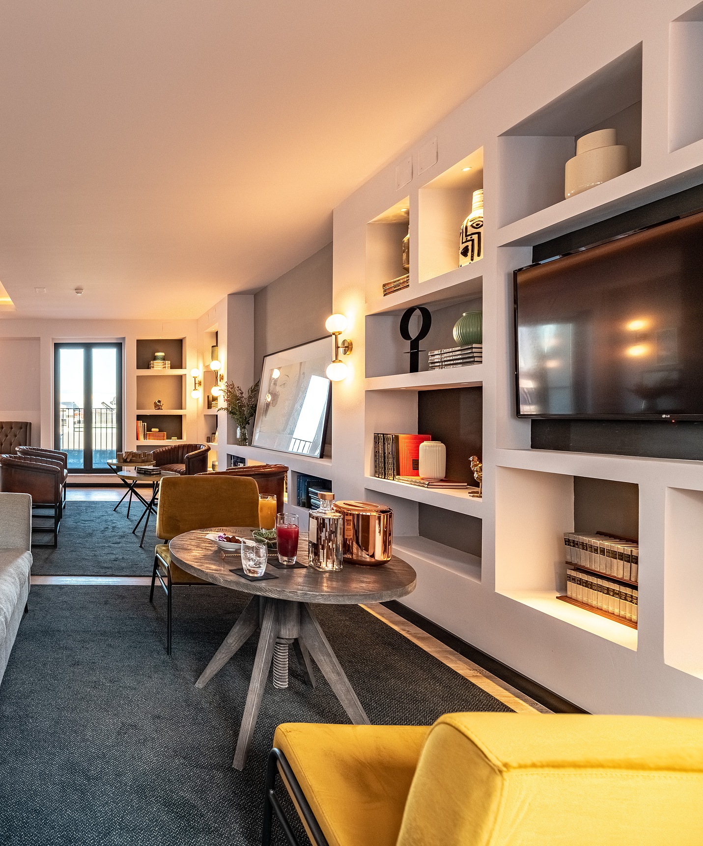 Lounge con sofás, sillas, mesas, cuadros, televisión, alfombras y objetos de decoración con ventanas con vista a la ciudad
