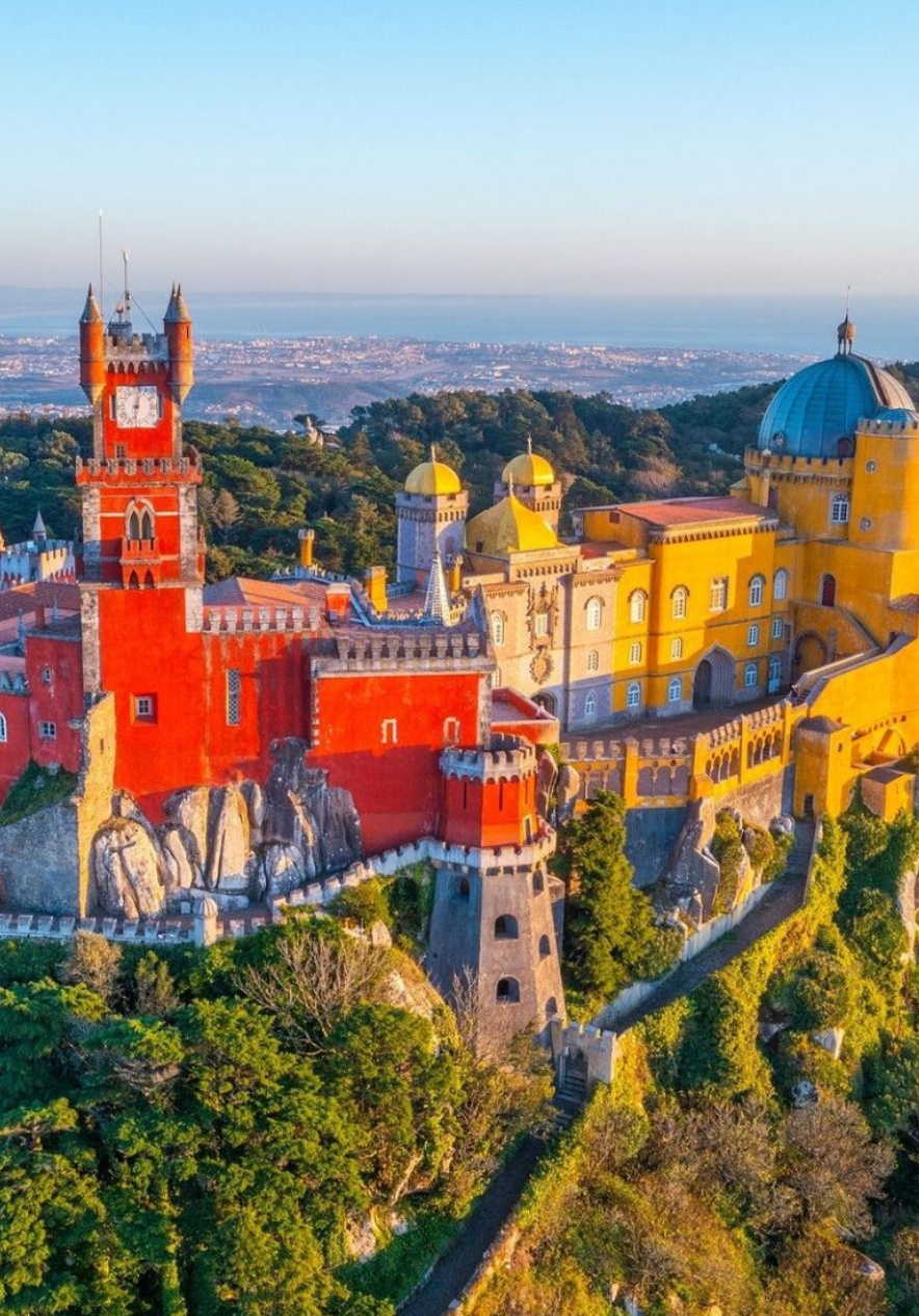 Vista panorámica del Palacio da Pena en Sintra, con sus fachadas en tonos rojo y amarillo y el mar al fondo