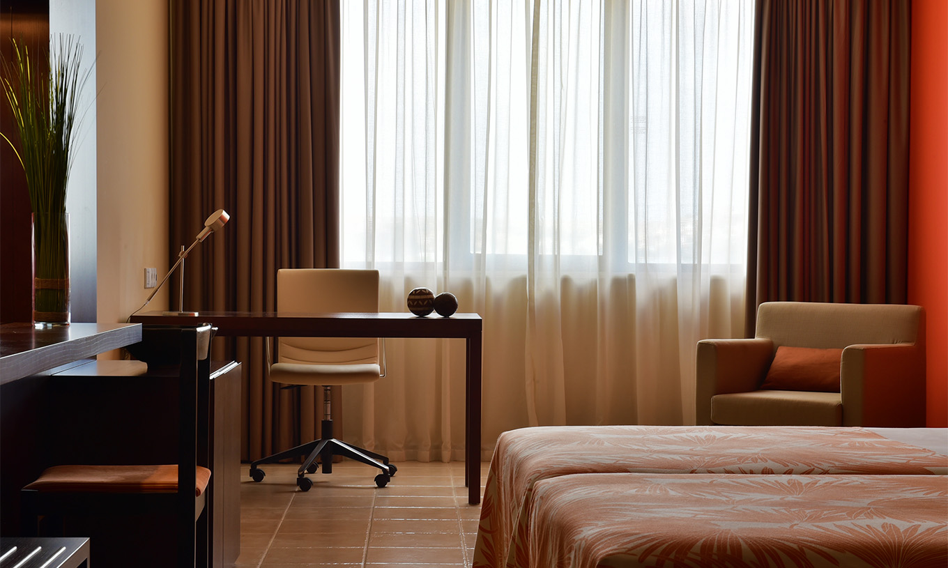 Le Chambre Standard du Pestana Tropico comprend un bureau avec lampe et une chaise, et un fauteuil