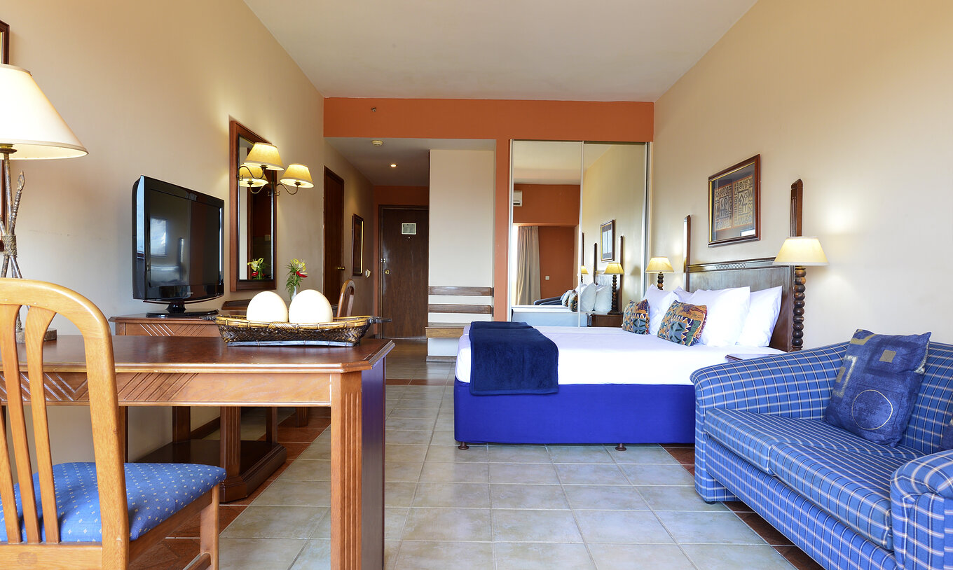La Suite Exécutive Familiale du Pestana Rovuma a un lit double, une armoire avec miroir, une télévision et un canapé