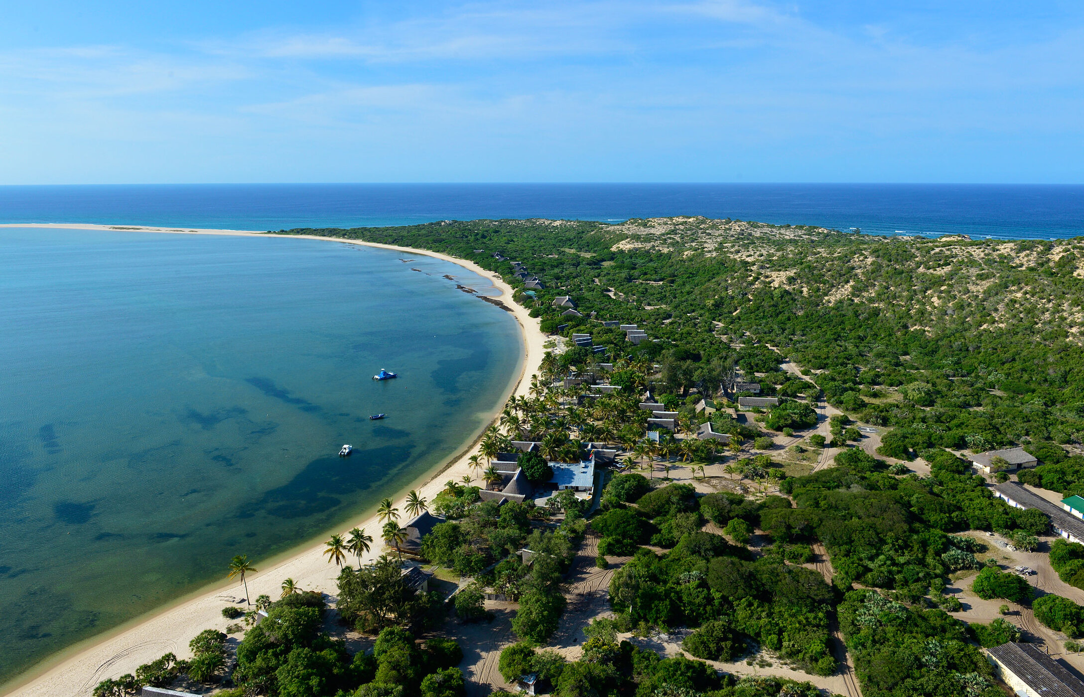 Vue aérienne de l'île de Bazaruto au Mozambique, avec une plage de sable blanc, entourée de végétation et quelques bâtiments.