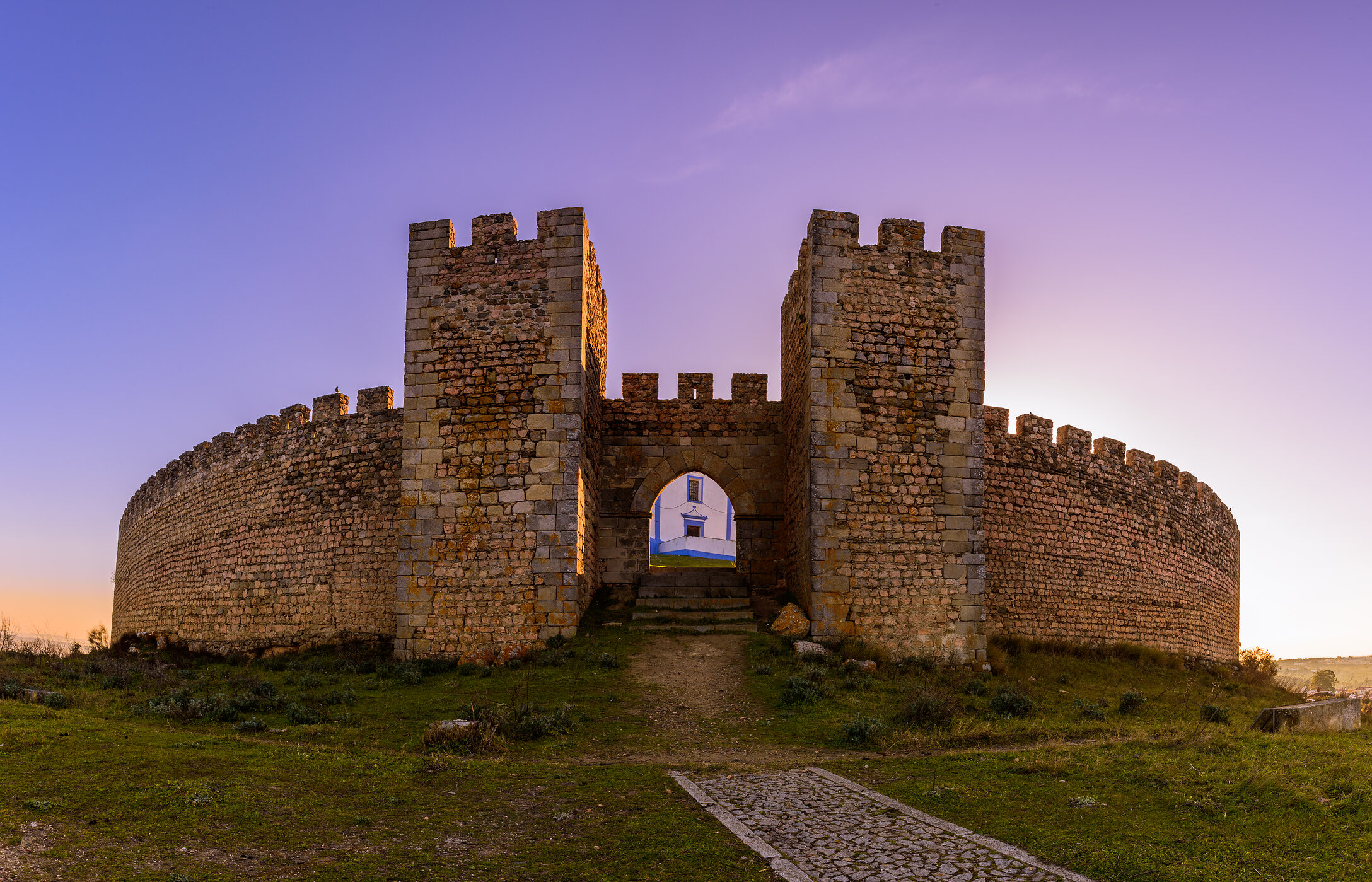 Vue frontale imposante de l'entrée du château d'Arraiolos, avec des murs en pierre et de la végétation autour