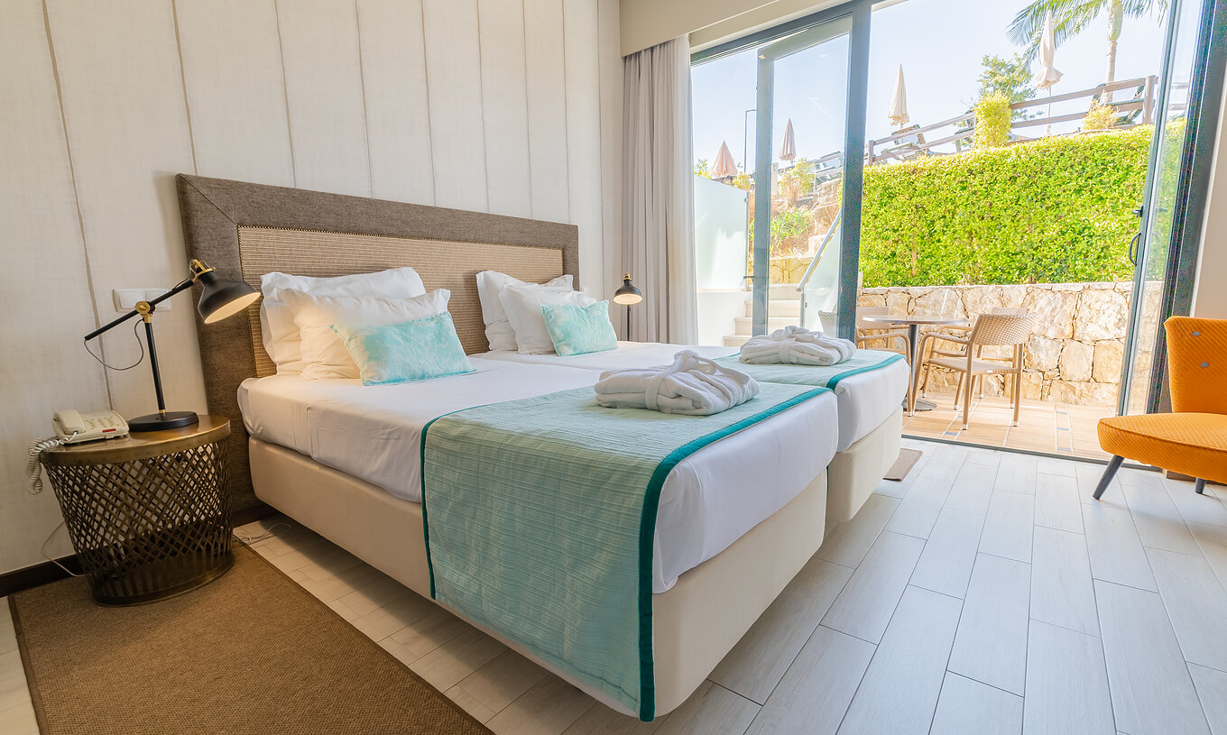 La Suite Garden du Pestana Alvor Park a deux lits, fauteuil, rideaux et balcon avec table et chaises