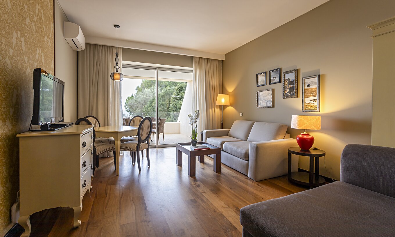 La suite Cliff T1 du Pestana Alvor Praia a un salon avec 2 canapés, une commode avec TV, une table à manger et des chaises