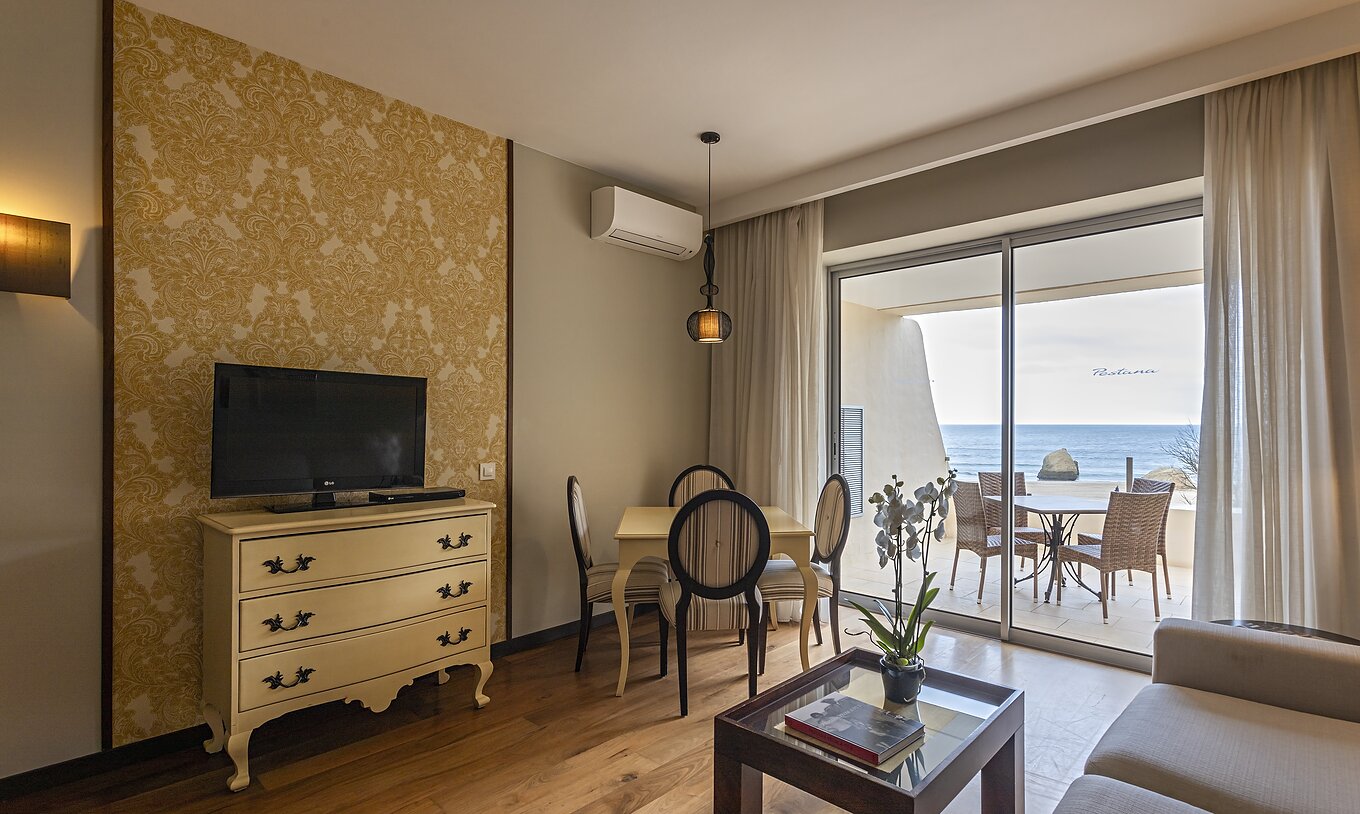 La suite Cliff T1 du Pestana Alvor Praia a un salon avec TV et un balcon avec table, chaises et vue sur la mer